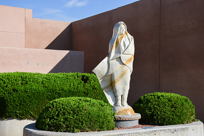 The morning sun illuminates the face of “White Deer of Autumn,” a sculpture by Denny Haskew, while creating stark shadows on the adobe walls behind it in the outdoor courtyard at The University of New Mexico-Gallup campus on July 18, 2024.