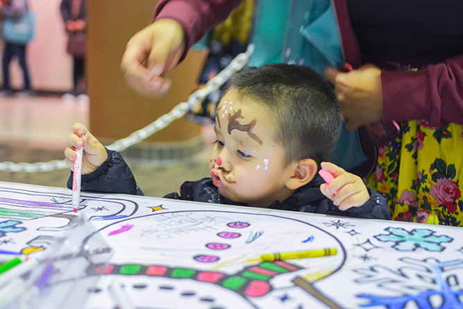 In this Dec. 5, 2024, photo, a young guest with his face painted colors a giant poster during Holiday in New Mexico at The University of New Mexico-Gallup.